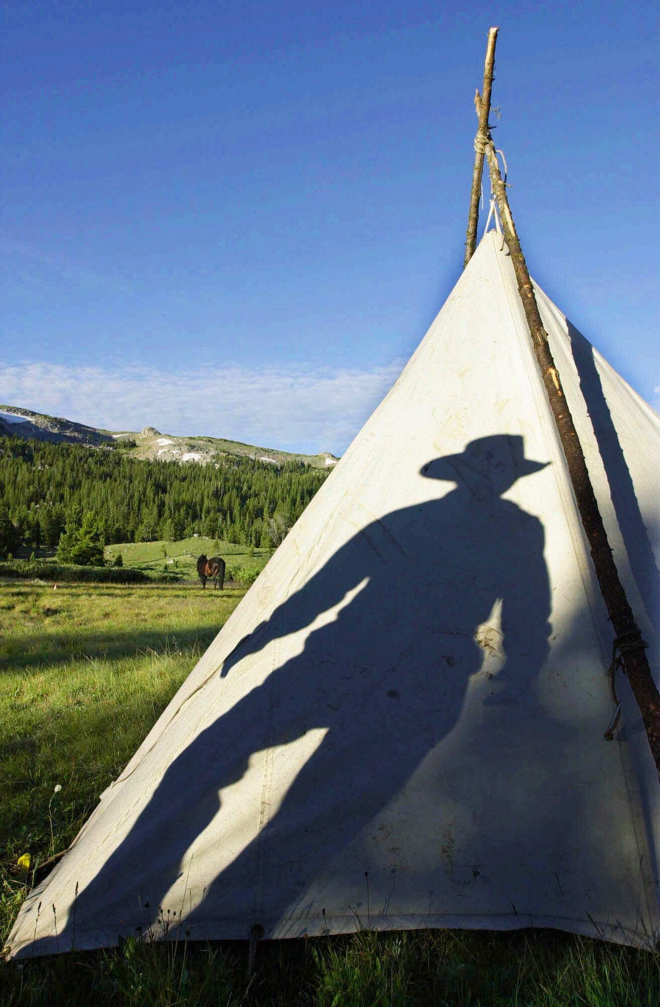 The rising sun casts the shadow of outfitter Judy Inberg on her teepee as she prepares for a morning ride during a pack trip in the Shoshone National Forest in Wyoming July 7, 2001. The forest, which is part of the greater Yellowstone ecosystem, was opened to oil and natural gas drilling. Wildlife experts fear that expanding operations in the area will affect the grizzly bear and wild game herd populations.  Shoshone National Forest