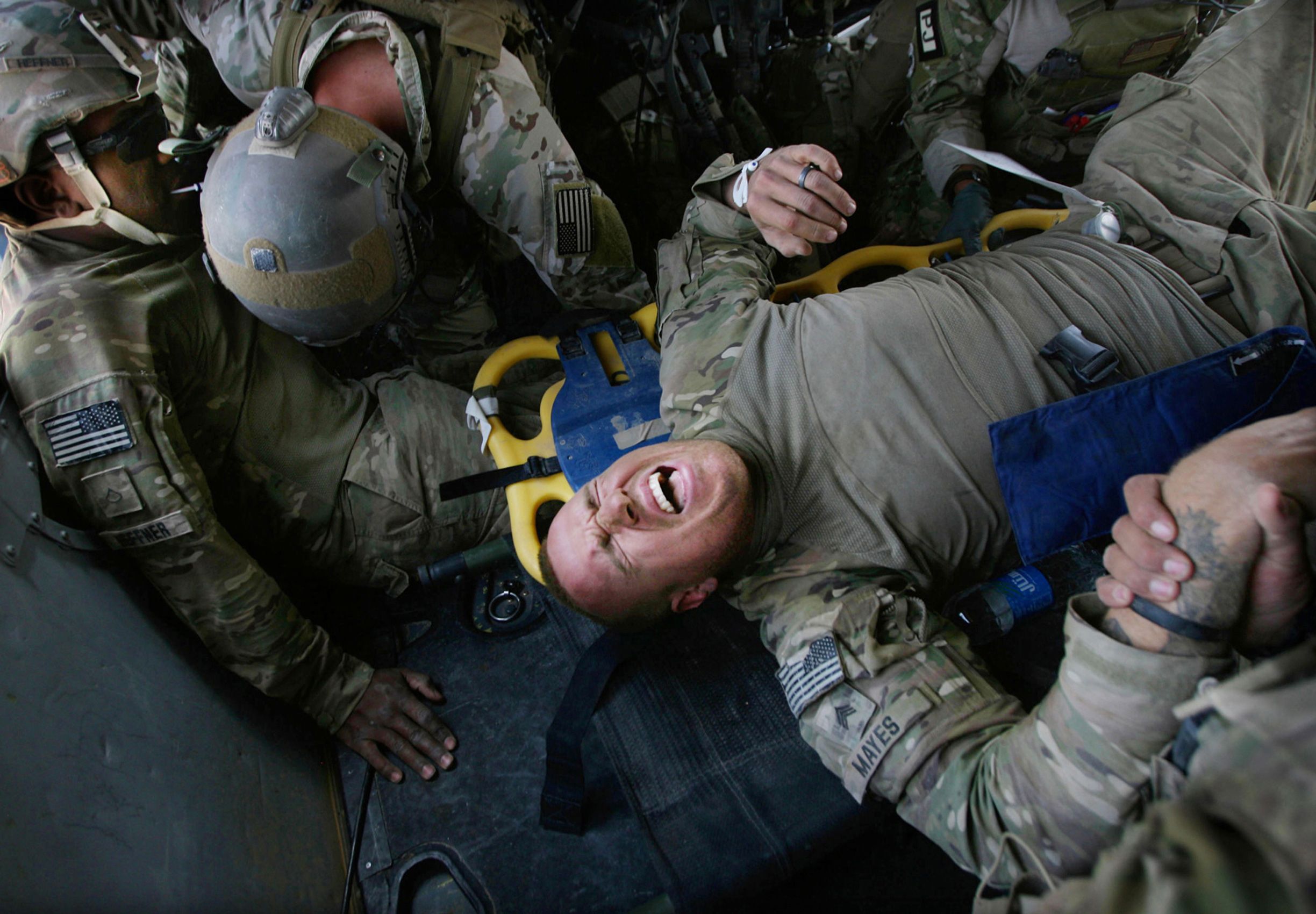 Army Sgt. Wyatt Mayes grimaces as a back brace is moved underneath him while Air Force Pararescueman Master Sgt. Bill Strouse, center, listens to Army Pfc. James Heffner, left. Both soldiers were wounded in an improvised explosive device attack in Helmand province on June 24, 2012.  Air Force Pararescue