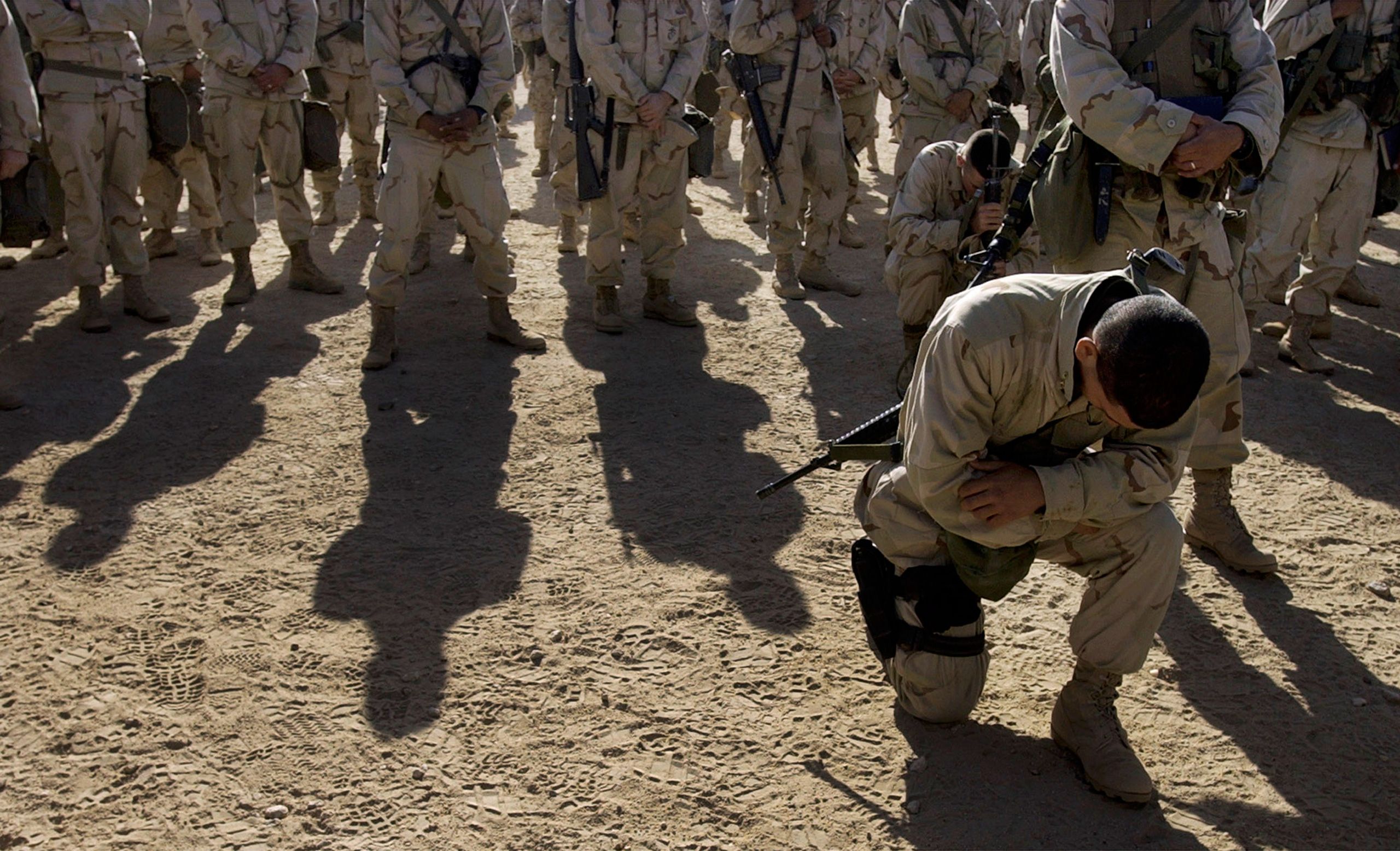 A marine kneels after receiving communion during a catholic mass for the 1st Marine Expeditionary Force at Life Support Area 7 in the Kuwaiti desert south of Iraq on Sunday, Feb. 23, 2003.  Invasion of Iraq