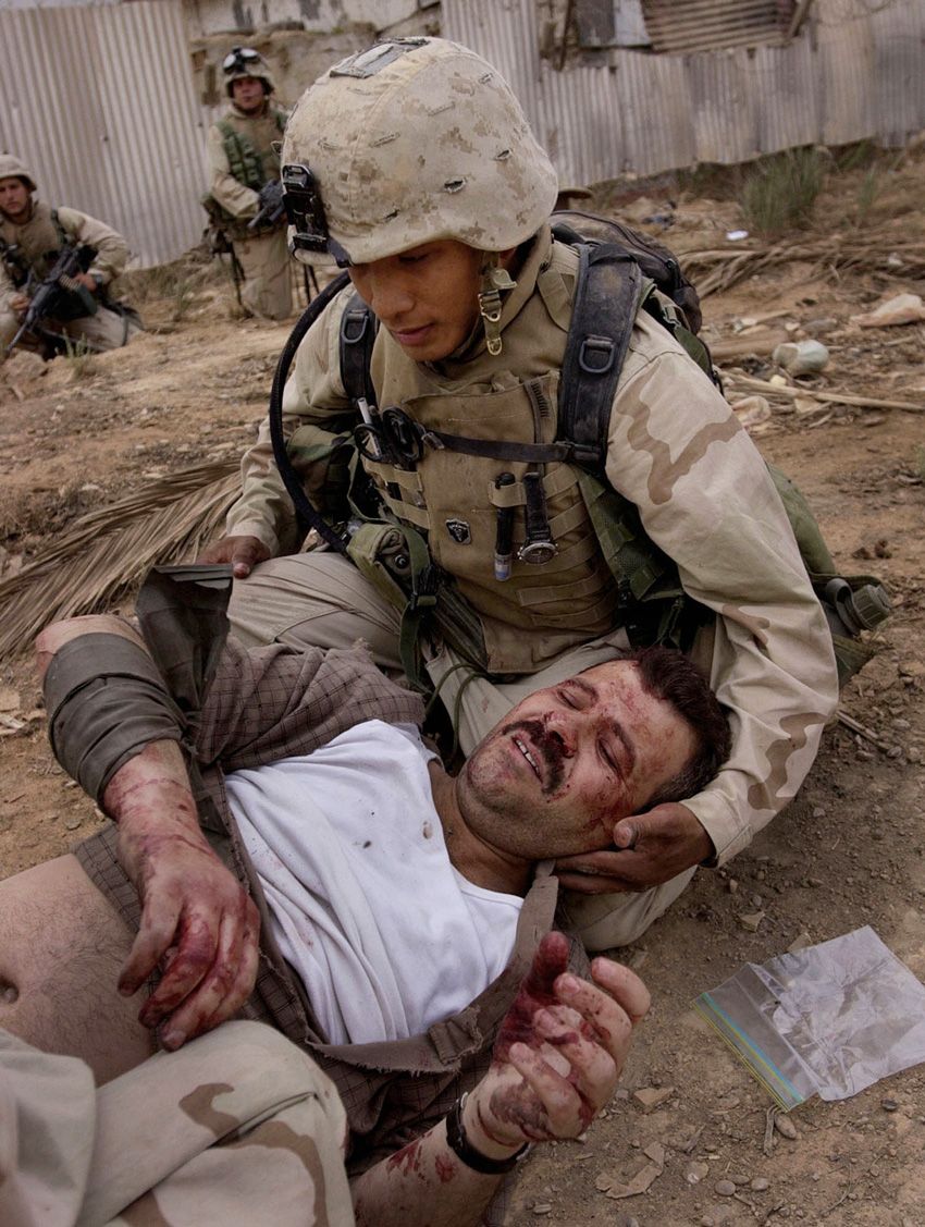 Navy corpsman Romualdo Humarang, of San Diego, attends to a wounded Iraqi man after the bus the man was riding in came under fire as it entered a military compound that U.S. Marines had recently taken in southeast Baghdad on Tuesday, April 8, 2003.  Invasion of Iraq