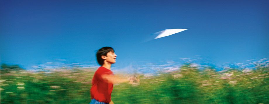 Boy flying a paper airplane.