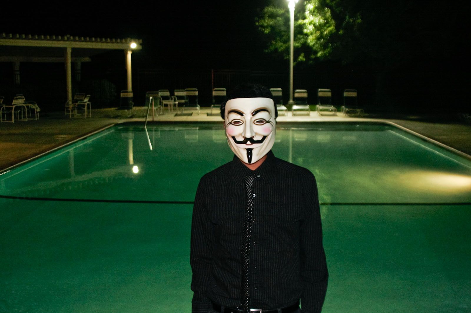 abstract editorial portrait of young man at night by pool side with Vendetta mask-paolophoto.com/mask/San Francisco/photo.jpg in black shirt at party in San Francisco Bay Area,California by San Francisco advertising photographer PaoloPhoto. V for Vision_Man in the Mask-paolophoto.com/mask/San Francisco/photo.jpg