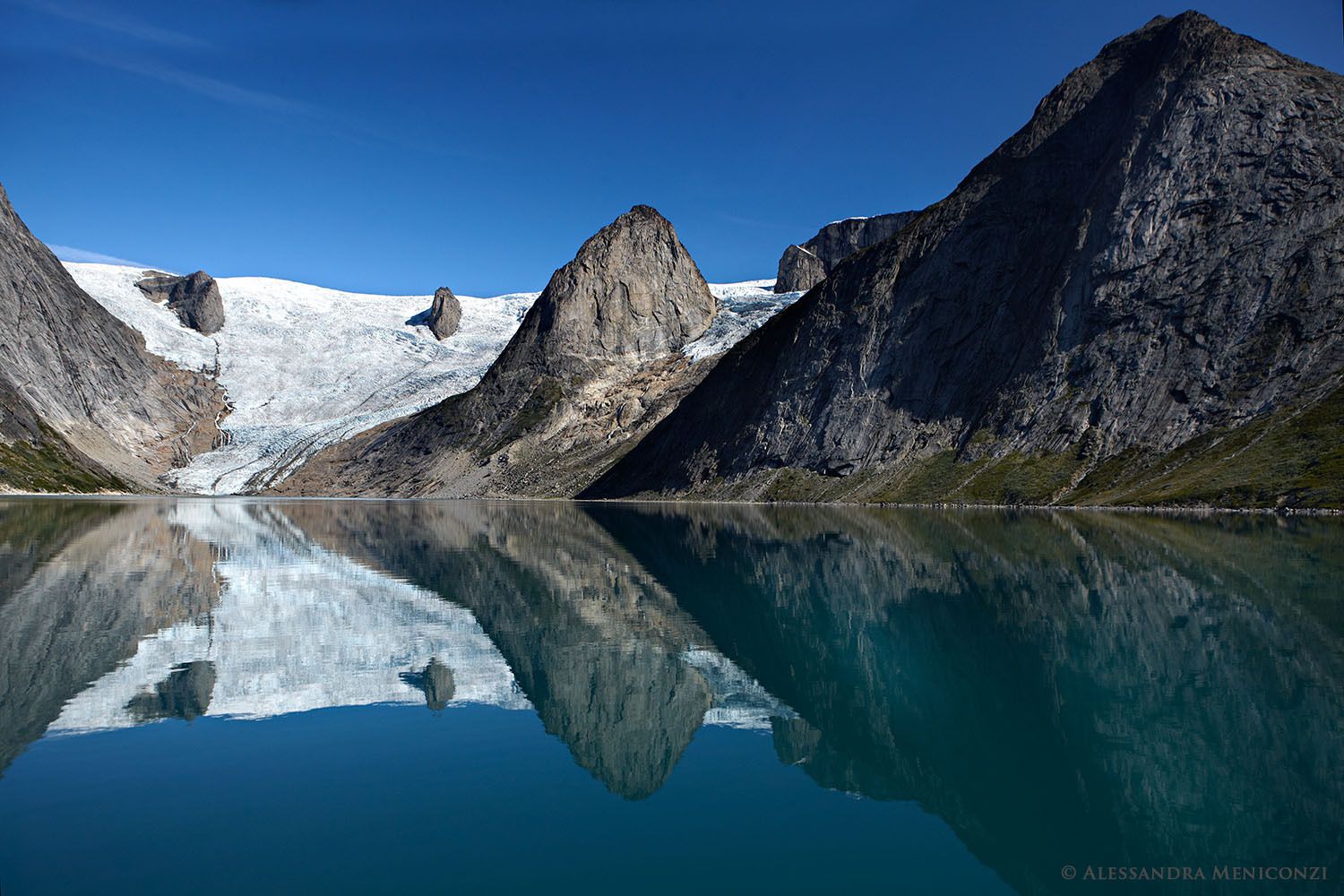 A receding glacier and pinnacle peaks are reflected in the still water of Tasermiut Fjord, South Greenland.