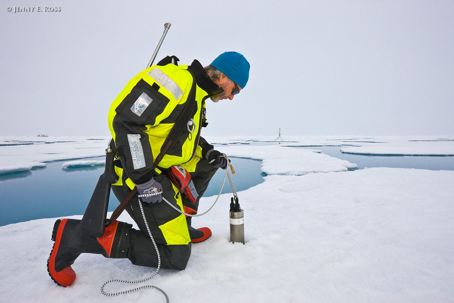 Norwegian Polar Institute geophysicist Arild Sundfjord, a physical oceanographer, deploys a scientific device through a hole in Arctic sea ice during a research expedition. The device is a "CTD", which detects conductivity, temperature, and depth in the ocean beneath the ice. The device’s primary function is to collect data within the water column that can be used to evaluate how the temperature and salinity of the seawater change with depth at a particular location. This work occurred on a large floe of melting summer sea ice in the Arctic Ocean as part of NPI's 2012 "ICE" (Ice, Climate, and Ecosystems) expedition. The NPI research ship "RV Lance" was attached securely to this particular floe of ice, and the vessel moved with the floe as the ice floated freely in the ocean, for the duration of various on-ice research activities in July-August 2012. Dr. Sundfjord is armed with a rifle and a flare gun (the latter is in the red pouch at his waist) to protect himself and his colleagues Scientific research on arctic sea ice, central polar basin, Arctic Ocean