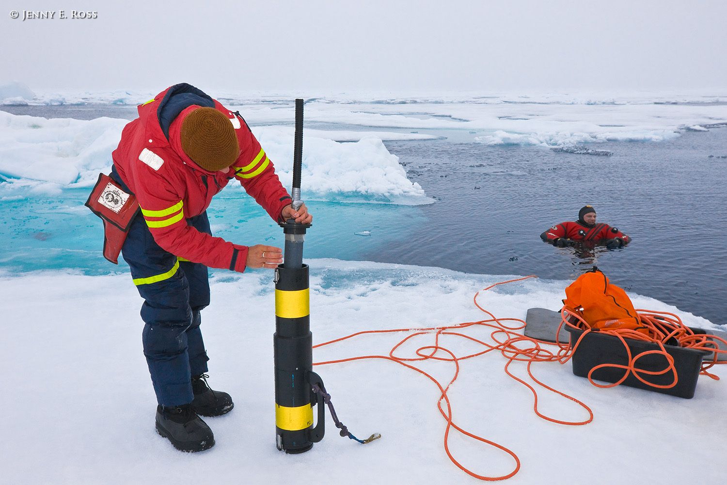 Norwegian Polar Institute ICE technician Jago Wallenschus prepares equipment for underwater research activities at a large floe of sea ice in the Arctic Ocean during NPI's 2012 "ICE" (Ice, Climate, Ecosystems) expedition in July-August 2012. NPI scientific diver Rupert Krapp is in the water, ready to deploy the equipment for collection of water and biota samples. Scientific research on arctic sea ice, central polar basin, Arctic Ocean