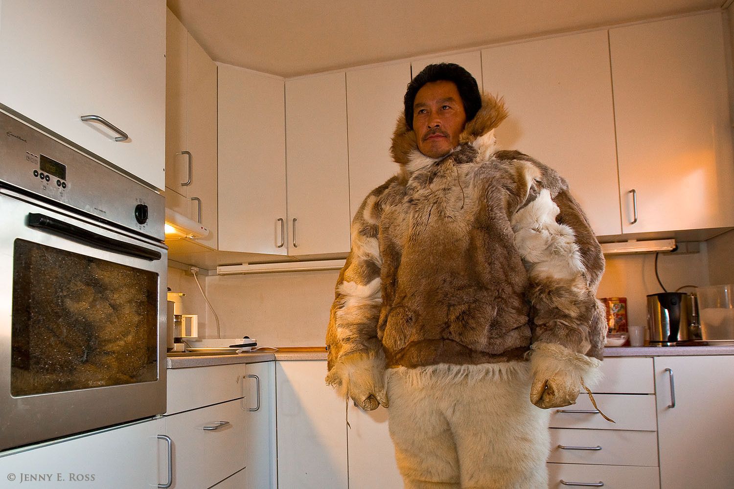 Inuit hunter Kristian Eipe wearing the tradtional clothing he uses when on a hunting expedition, in the modern setting of his home in Qaanaaq, Northwest Greenland.