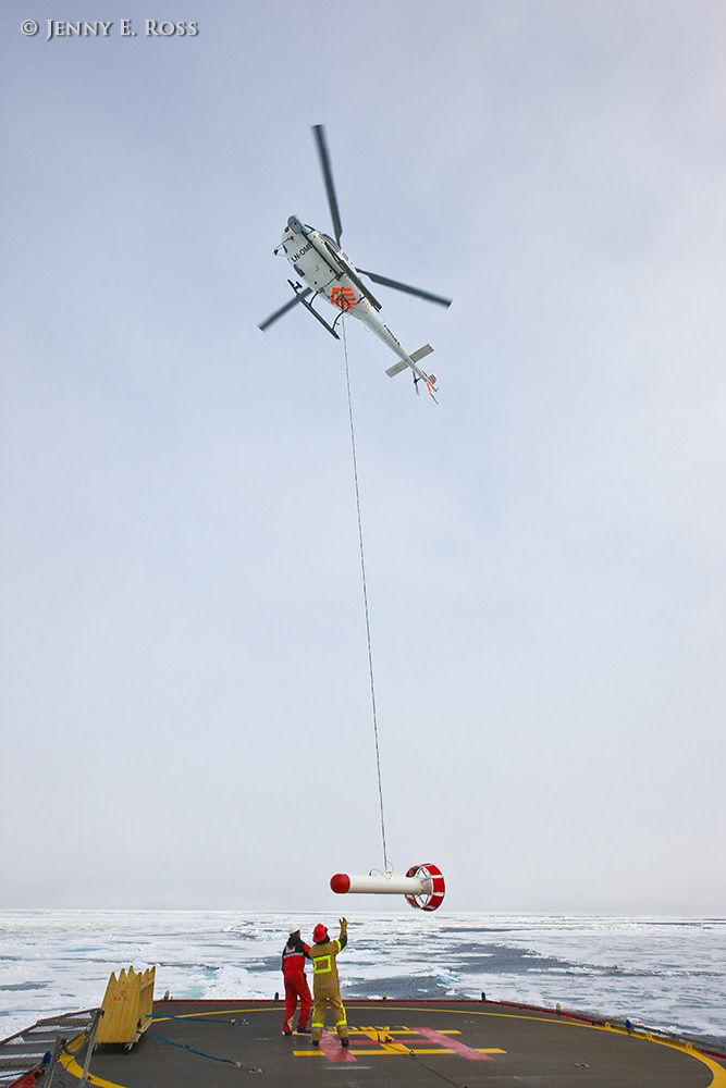 On a research expedition in the Arctic Ocean, Norwegian Polar Institute scientists assessed sea ice thickness using an airborne instrument called the EM-Bird, a large torpedo-shaped scientific device. During helicopter transects flown above the ice, the electromagnetic and laser sensors in the EM-Bird collect data for use in calculating the thickness of the sea ice. This work was conducted on melting summer sea ice in the Arctic Ocean as part of NPI's 2012 "ICE" (Ice, Climate, and Ecosystems) expedition in July-August 2012. In this photograph, the helicopter carrying the EM-Bird is approaching the RV Lance to land on the ship after doing transects to collect data. Scientific research on arctic sea ice, central polar basin, Arctic Ocean