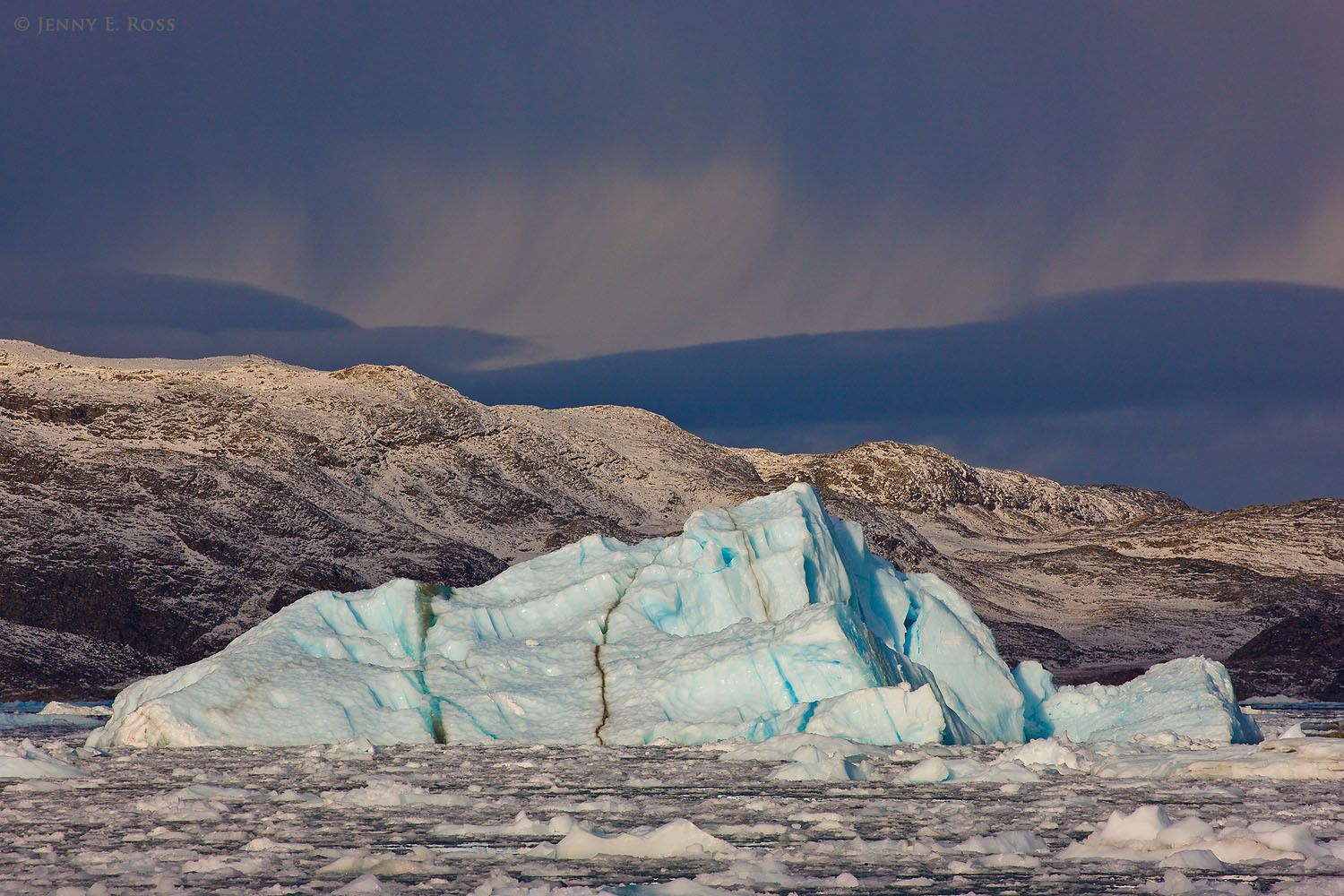 A melting iceberg in brash ice, with a distant rainstorm approaching, near Kangilerngata Sermia Glacier, West Greenland.