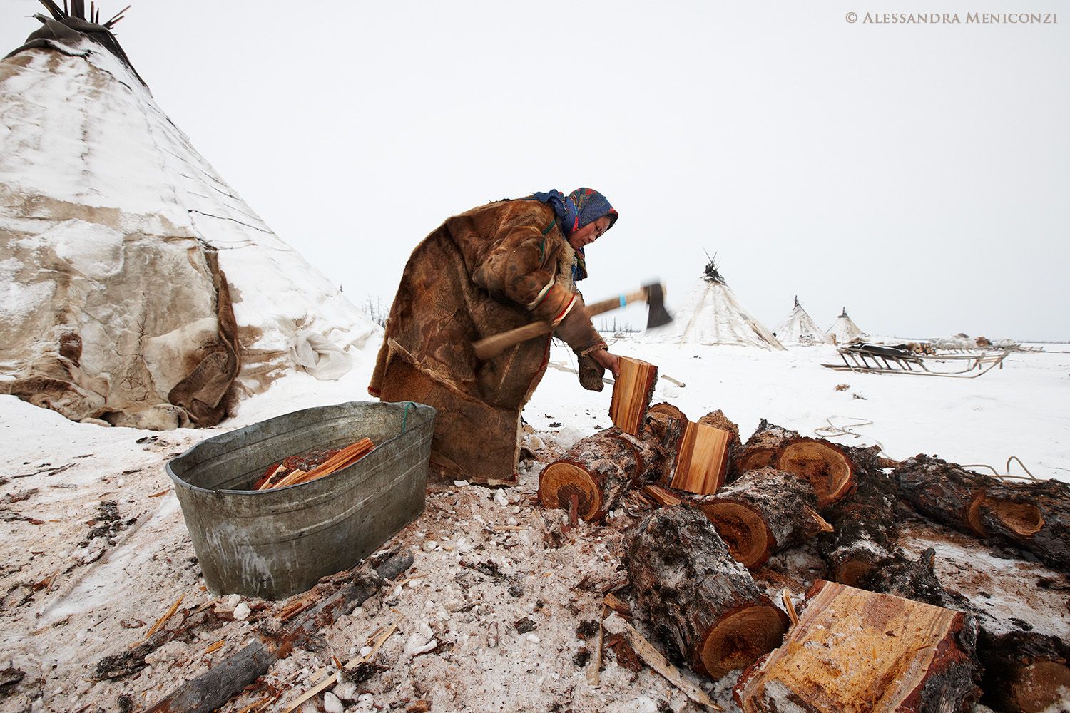 Yamal Peninsula, Siberia, Russian Federation. A Nenet woman chops firewood outside her family's chum at a winter camp.