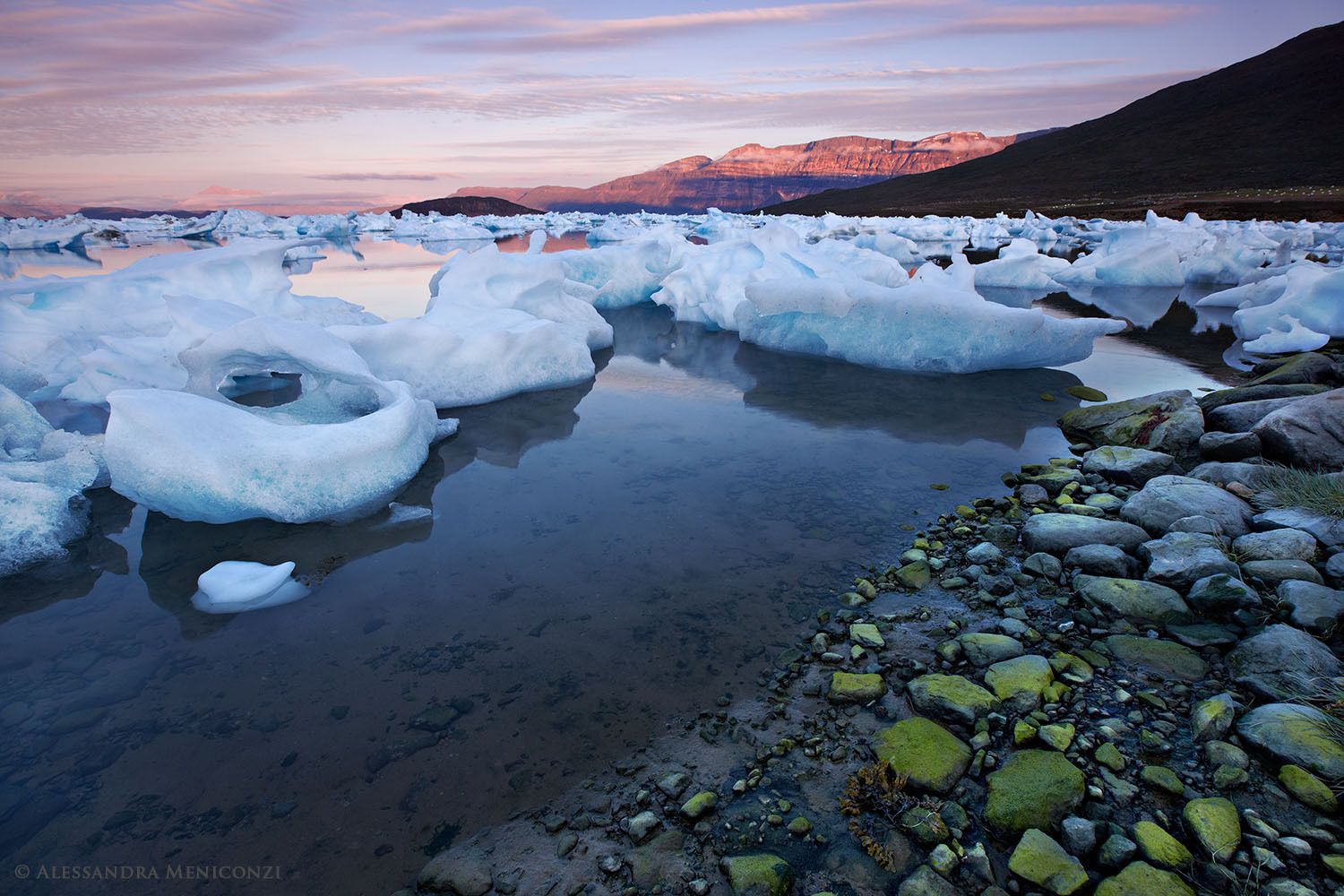 Following two days of strong foehn winds, numerous large chunks of ice are stranded ashore and grounded in shallow water in Sermilik Fjord, southeast Greenland.
