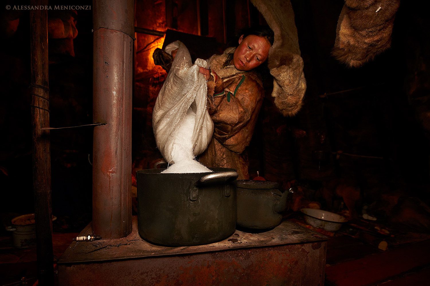 Yamal Peninsula, Siberia, Russian Federation. Inside her family's chum, a Nenet woman empties snow into a pot to make fresh water for cooking.