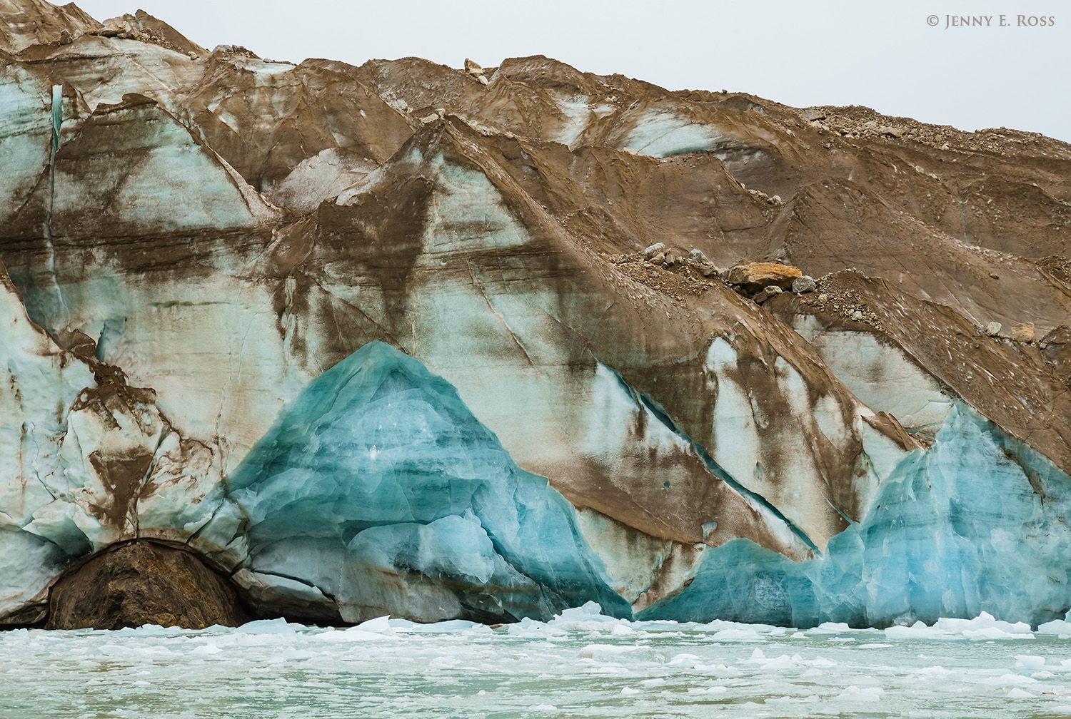 As the ice of Sefstrom Glacier melts and recedes, its surface is increasingly coated with residual dirt and rock debris. Clean blue ice is exposed where icebergs have broken off the glacier face.