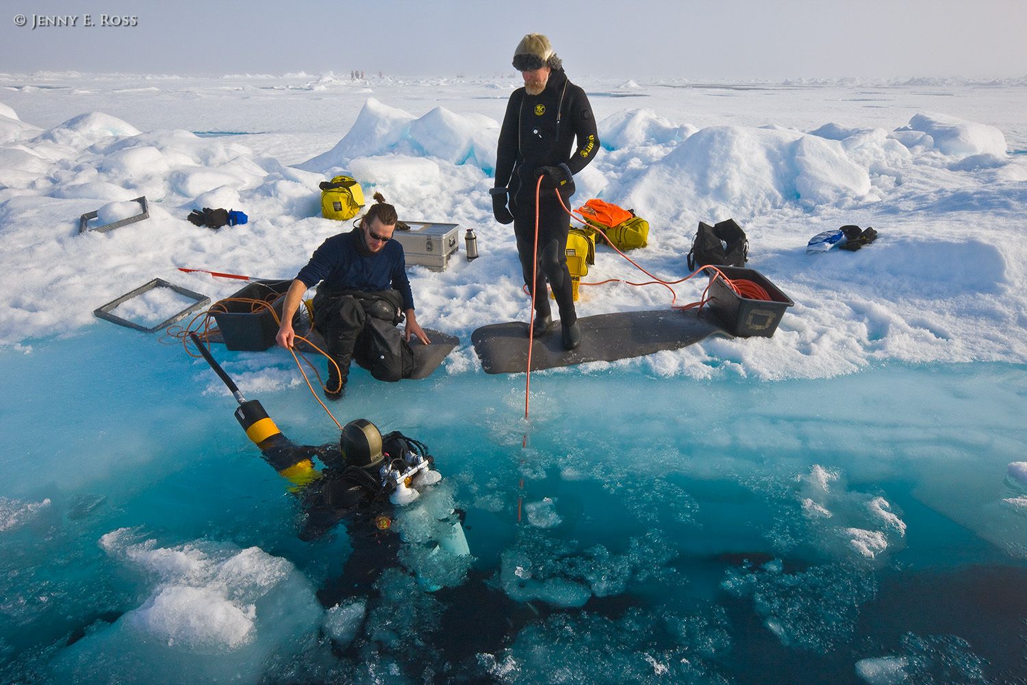 Norwegian Polar Institute scientific diver Michal Tessman prepares to dive using a vaccum device to collect ice algae, phytoplankton, and zooplankton samples beneath the Arctic sea ice. He is assisted by NPI marine ecologist and diver Haakon Jop (standing on right) and NPI diver Peter Leopold (sitting on left). The research activities occurred on a large floe of sea ice in the Arctic Ocean during NPI's 2012 "ICE" (Ice, Climate, Ecosystems) expedition in July-August 2012. Scientific research on arctic sea ice, central polar basin, Arctic Ocean