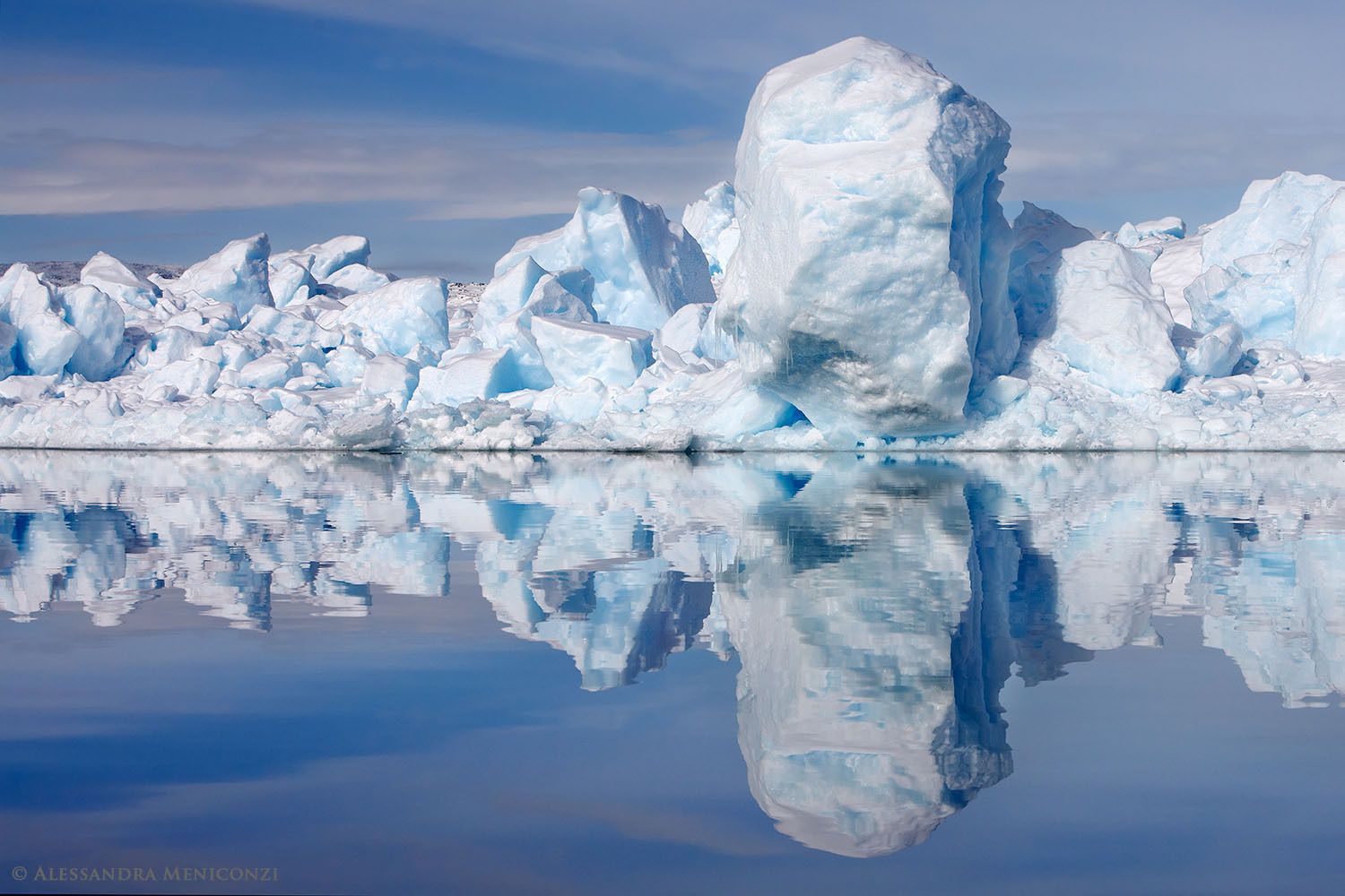 A disintegrating iceberg is reflected in the still water of Sermilik Fjord, southeast Greenland.
