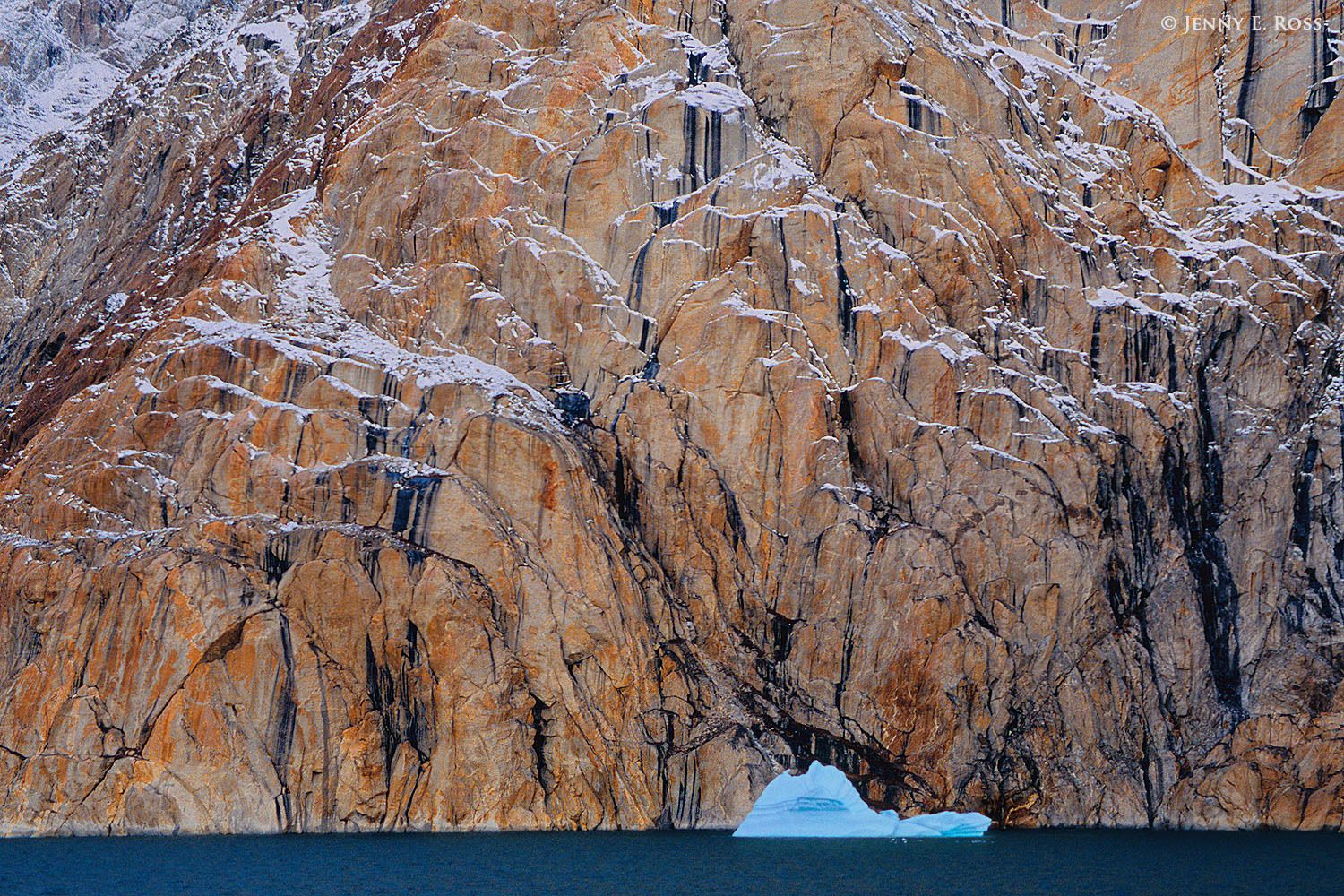Iceberg, and cliffs adorned with desert varnish and a dusting of snow, in Ofjord within Scoresby Sund, East Greenland.