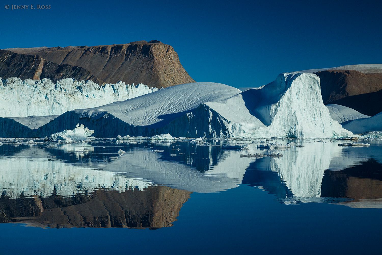 Icebergs, ancient metamorphosed sedimentary rock, and Daugaard-Jensen Glacier are reflected in the still water of Norvest Fjord in Scoresby Sund, Northeast Greenland National Park, Northeast Greenland.