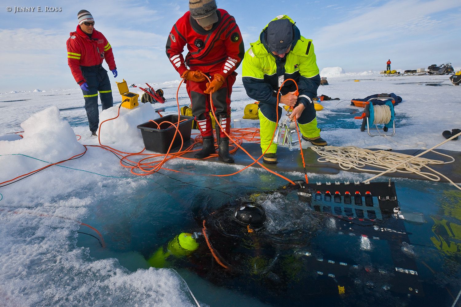 Norwegian Polar Institute scientific diver and Arctic marine ecologist Haakon Hop surfaces with a rack of seawater and ice algae samples that have been undergoing a timed incubation beneath a large floe of sea ice for an experiment relating to biological productivity in the Arctic Ocean. Dr. Hop is working with Dr. Philipp Assmy (in red on the left), an NPI biological oceanographer and plankton ecologist, NPI diver Rupert Krapp (center) and plankton ecologist Svein Kristiansen (on right). One of the aims of the experiment was to assess biological productivity beneath different ice types and thicknesses, and in varying light conditions. Samples of ice algae were initially harvested from under the ice in this location, and then treated with a chemical marker which enabled Dr. Assmy to quantify subsequent growth rates when the samples underwent timed incubation beneath the ice. Ice algae are a crucial foundational component of the Arctic food chain, and are threatened by loss of sea ice d Scientific research on arctic sea ice, central polar basin, Arctic Ocean