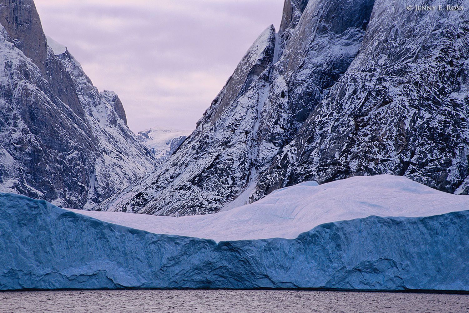 An enormous tabular iceberg floats by a jagged canyon that was once filled with a glacier in Ofjord within Scoresby Sund, East Greenland.