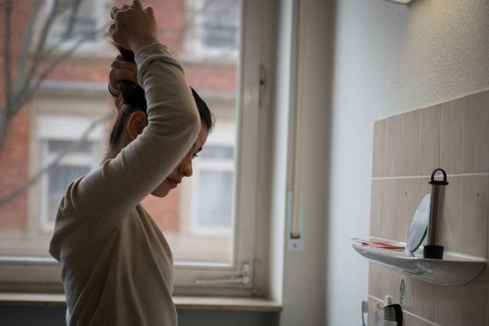 Sarah does her hair in her room in an apartment