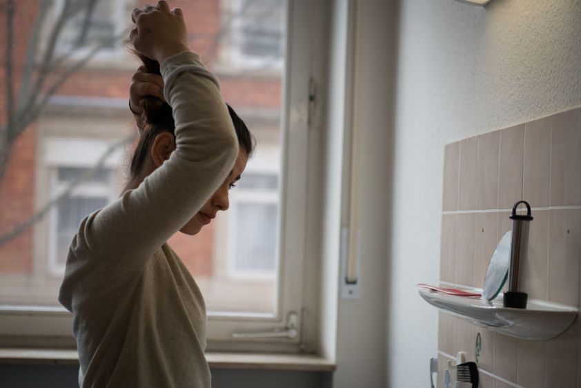 Sarah does her hair in her room in an apartment
