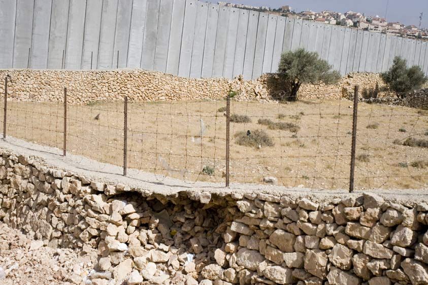 A stone wall made by Palestinian farmers is dwarfed by the Israeli segregation wall.  The settlement Gilo perches on the hilltop, it's area 'protected' by the segregation wall. 1pal_wallbthm_05_28