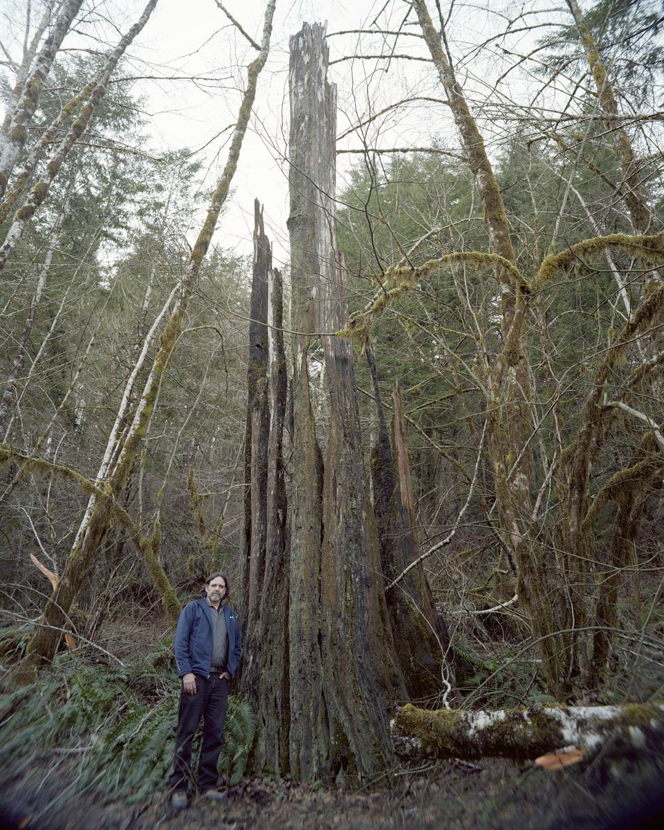 Chris Friend is the coordinator of the Tillamook State Forest Interpretative Center.  Chris has fought past fires throughout the west coast, and in this picture he stands next to a charred remnant of the Tillamook Burn.  Douglas Fir’s are exceptionally large trees, and while the re-forestation of the Burn has surpassed all expectations, it will take centuries to replace the dense stands of old growth trees which had once towered above the forest floor. Tillamook Burn, Oregon, Chris Friend, Tillamook Forest Interpretive Coordinator, Douglas Fir Snag