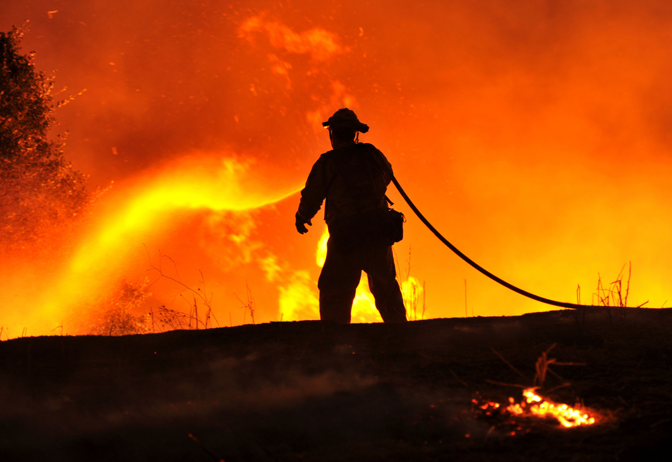 A lone firefighter sprays water on flames