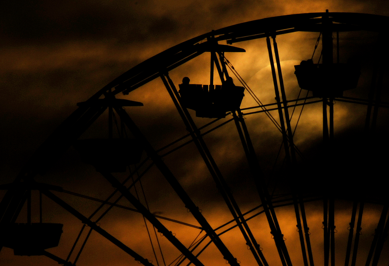 The sun sets behind clouds as people enjoy a Ferris Wheel ride at the Santa Monica Pier