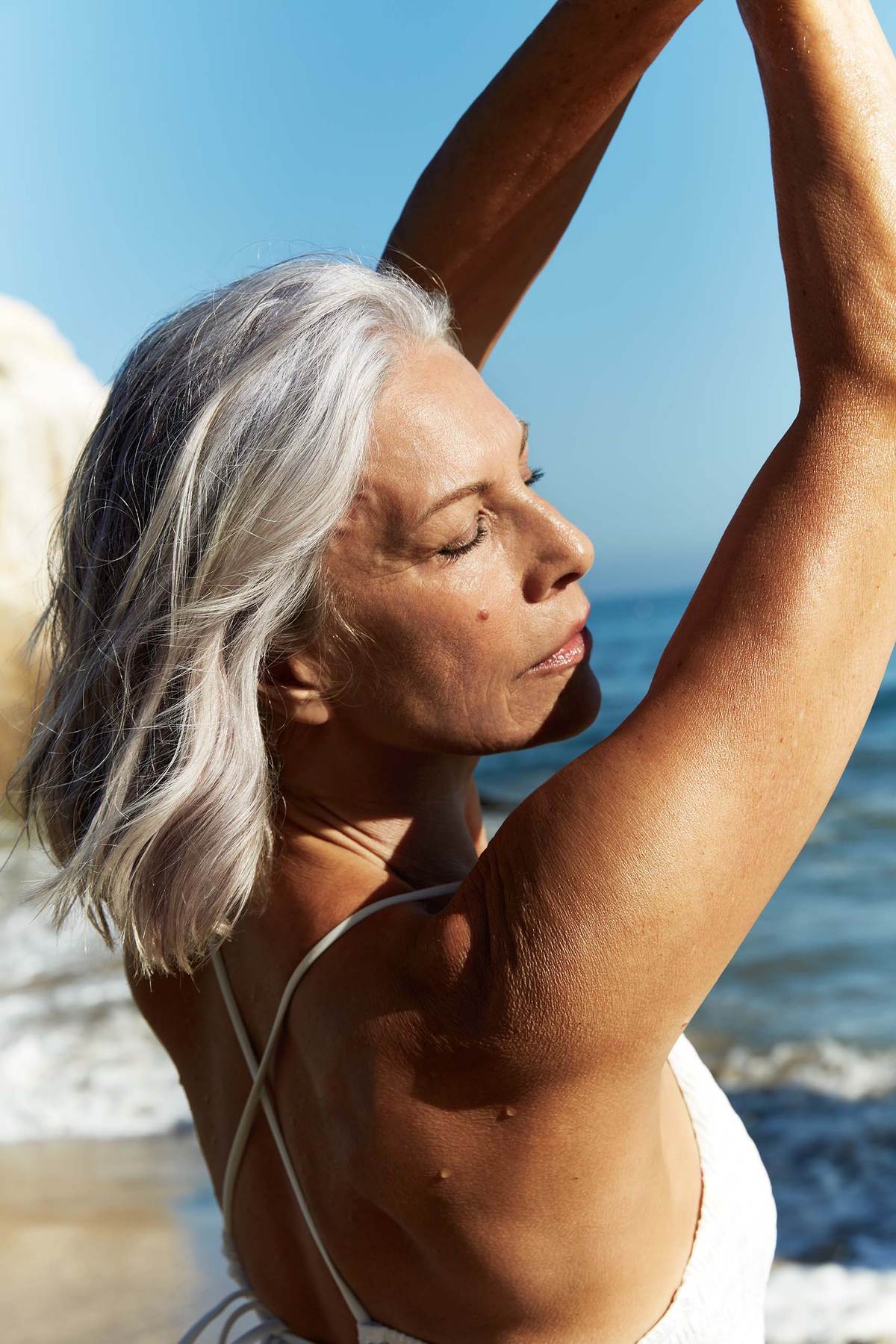 MATURE woman with raised arms wearing a swimsuit by the ocean