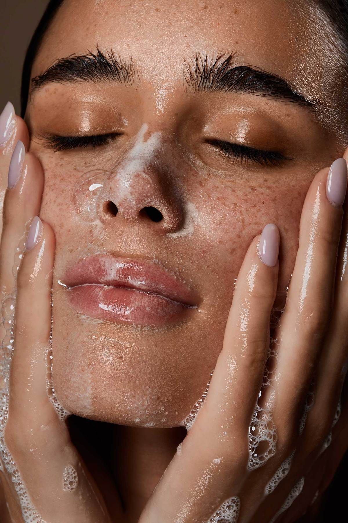  model with her eyes closed, foaming her face with soap