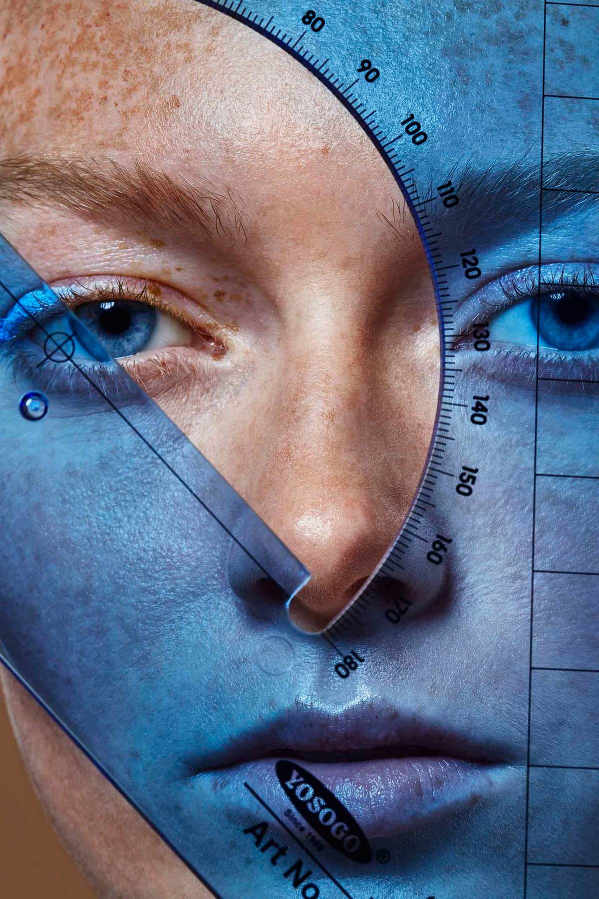 close up face of a model with freakles behind a BLUE plastic ruler 