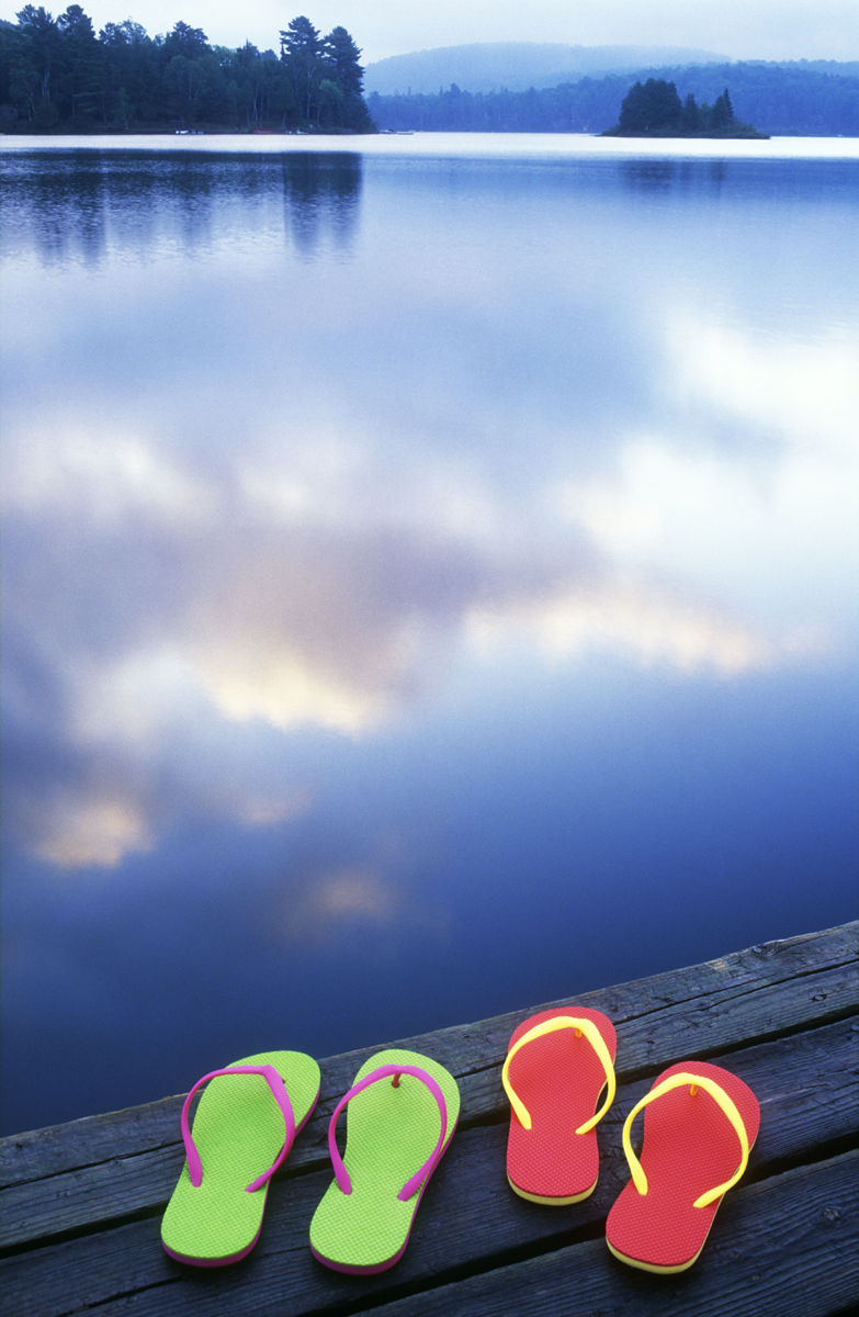 Oxtongue Lake, Ontario, Canada. Getty Images #200258193-001 Sandals on wooden pier with clouds reflected in lake, summer