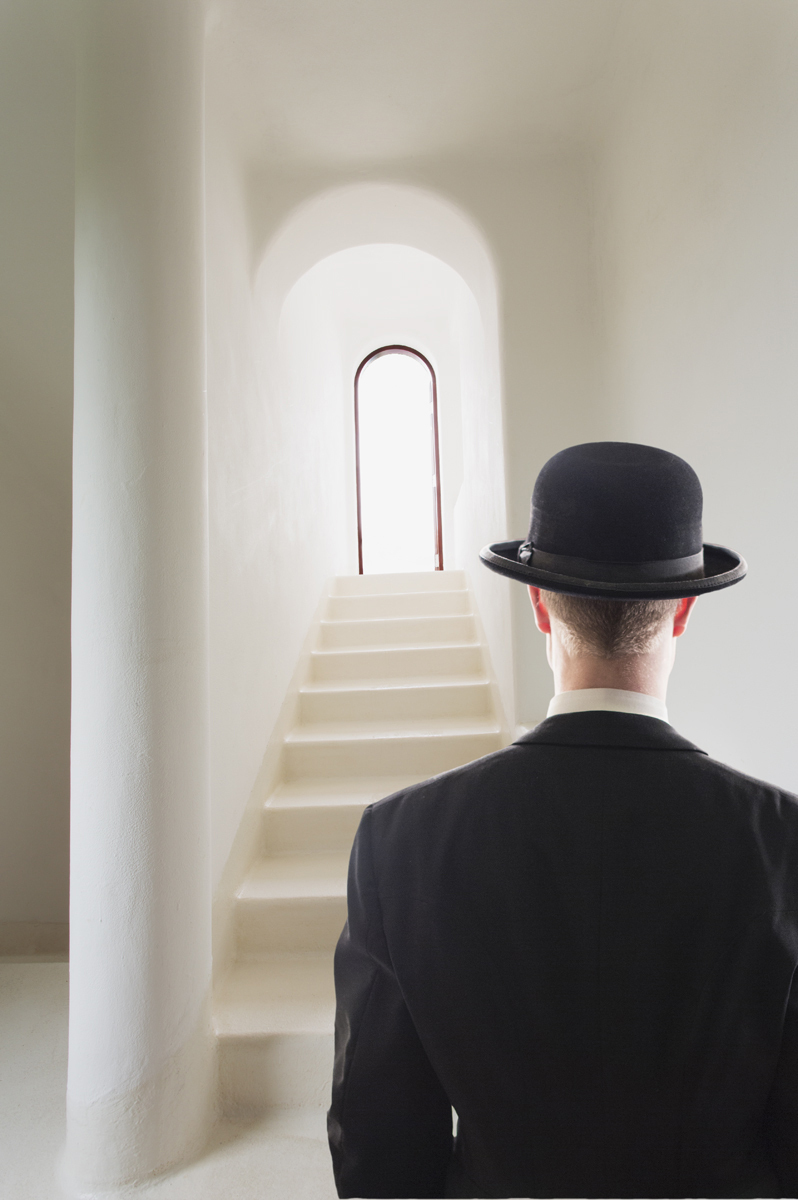 man in bowler hat and suit looking up at staircase steps leading to doorway