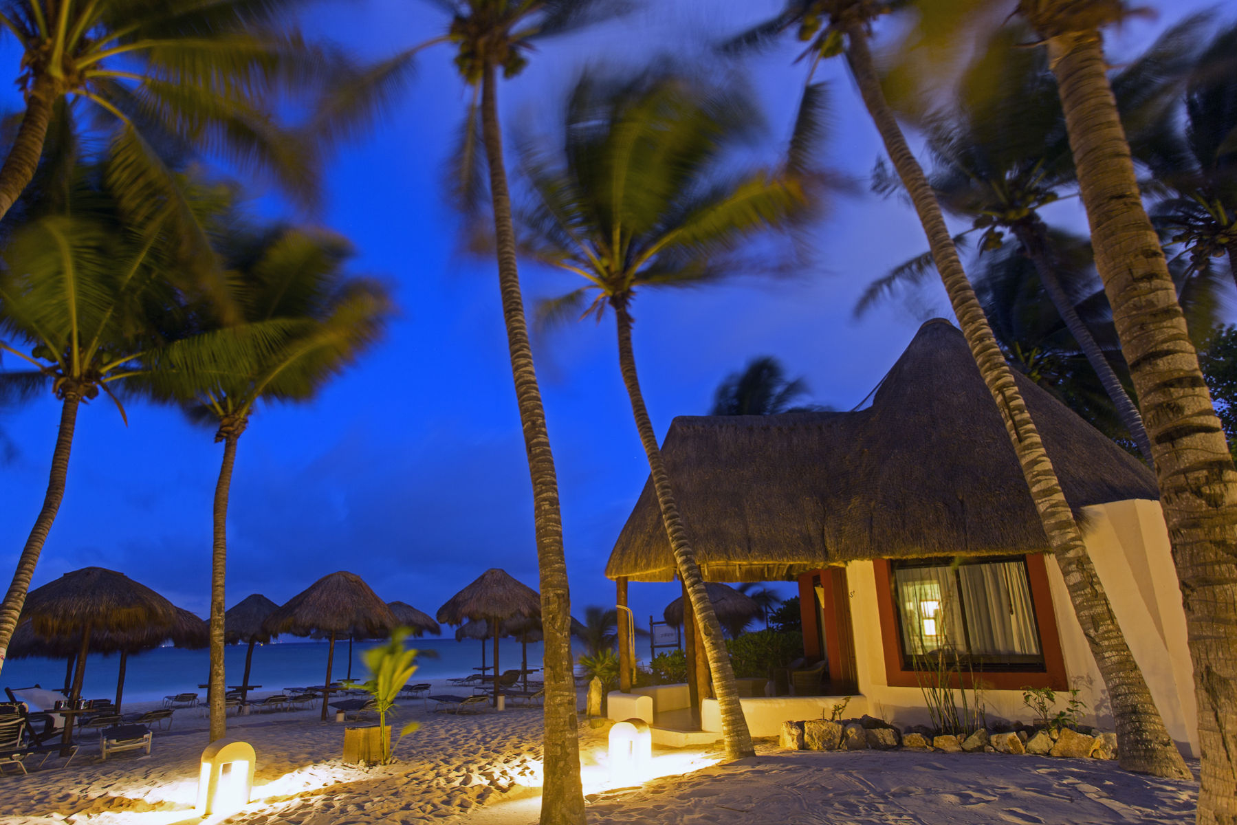 cabana style accommodation on the beach surrounded by palm trees at dawn Las Palapas Beach Resort