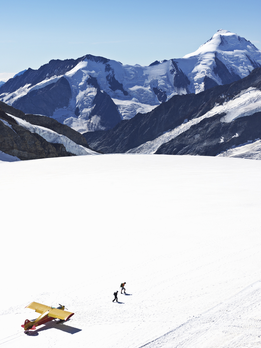 airplane on glacier  with mountains in background and two people walking away.The Great Aletsch Glacier, at 22 km the longest ice-stream (glacier) in the Alps, begins on the Jungfraujoch-Top of Europe. Getty Images #91954607 the Aletsch Glacier, mountains and airplane