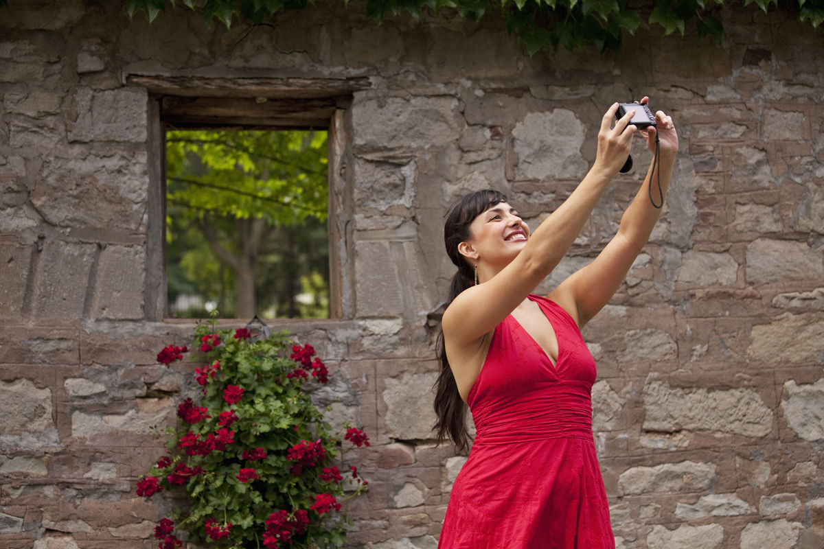 Canada,Ontario,Queenston. Woman taking self portrait against old stone wall with flowers Woman taking self portrait against old stone wall with flowers