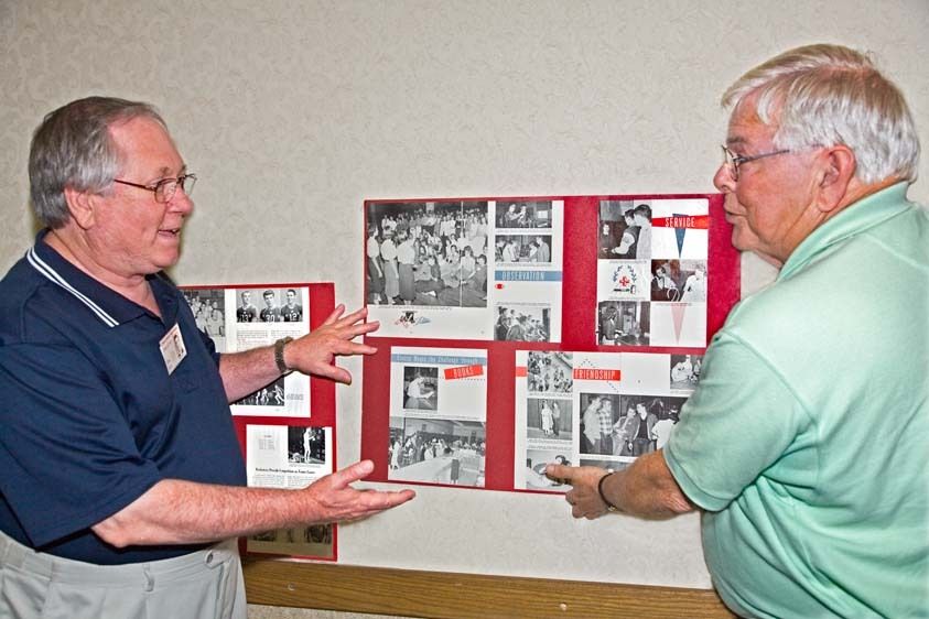 For 50th year reunion in Tulsa, OKlahoma, two senior men put up posters on wall of high school yearbook photographs and newspaper clippings Two senior men place old posters for 50th reunion on wall