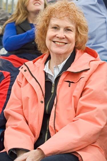 One mature female with red hair wears coat and sits in stadium watching game in early Spring in Mississippi Senior woman sits in grandstand smiling