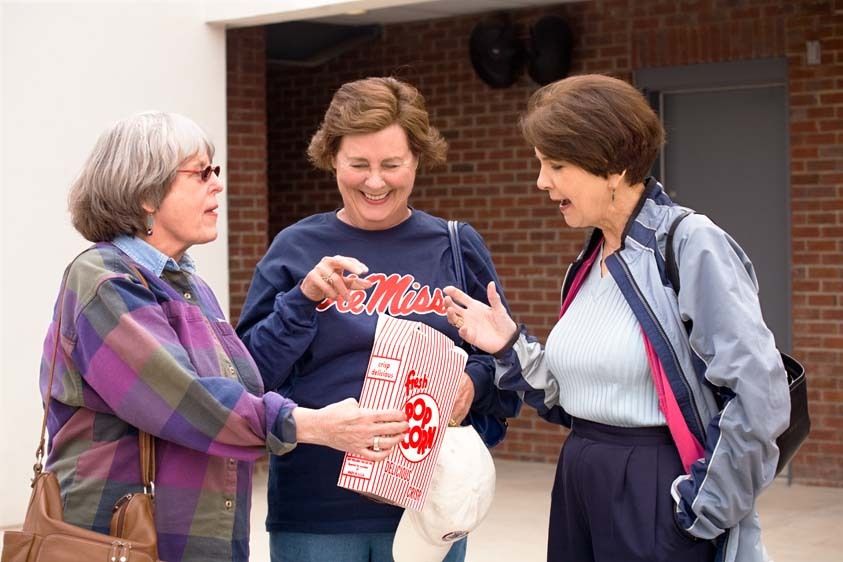 Three mature women with Ole Miss shirt enjoy popcorn at Mississippi University sport stadium in Oxford, Mississippi Three Senior Women reach for popcorn at stadium