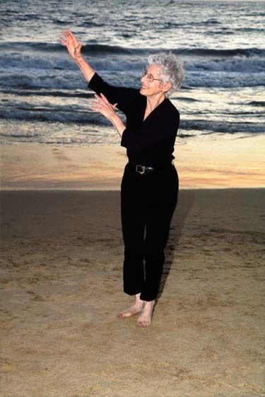 Senior female smiles dancing and exercising on the beach with waves behind her in Los Angeles, California One senior woman dance exercises on beach