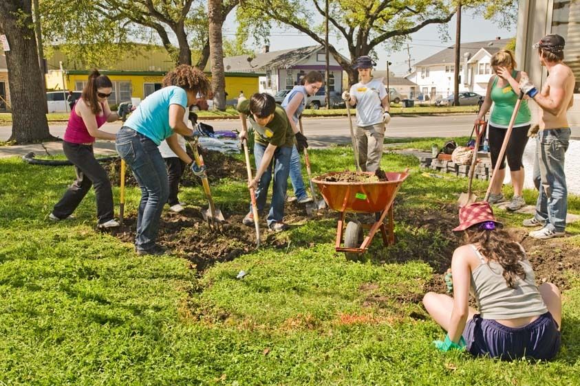 Young women and young men students volunteer to dig with shovels and load wheelbarrow in yard of New Orleans home in the 9th ward to make a water drainage method for houses Group of college teens volunteer outdoors in New Orleans