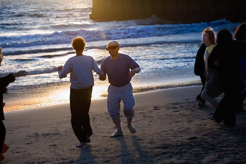 Older couple dances on beach with exercise class at sunset at Playa Del Rey Beach,California Senior man and woman dance on the beach at sunset
