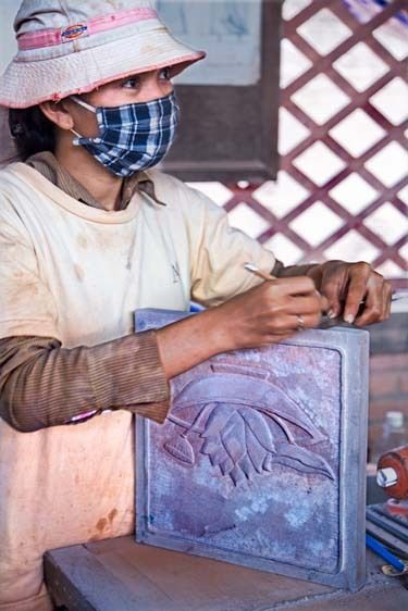 Young female artist with stone sculture of bas relief works with mask for protection and measures carving Cambodian woman measures and marks on stone carving