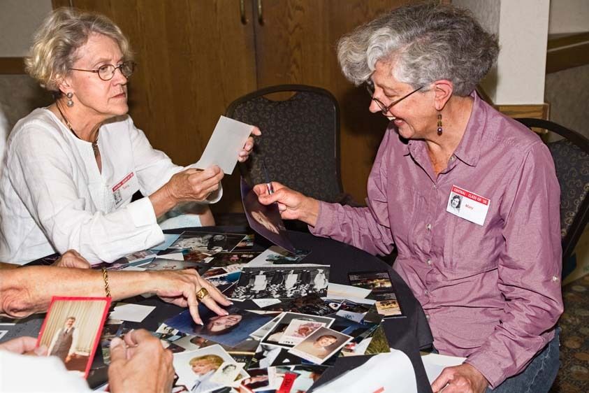 Two senior women look at photos from high school at reunion Two senior females look at photos on table at reunion