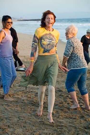 Woman instructor leads senior adults in exercise and dance class on Playa Del Rey Beach at sunset in Los Angeles, California Smiling senior women dance exercise on the beach