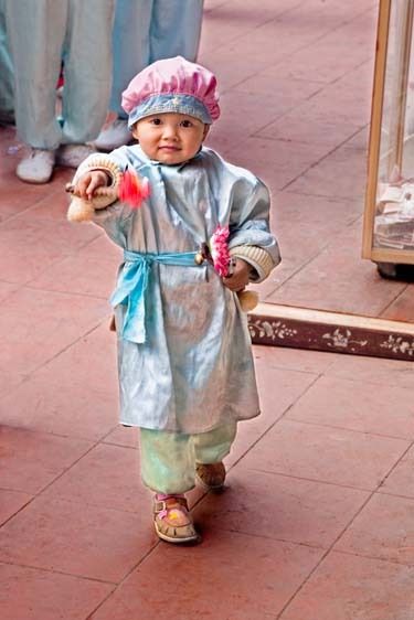 Vietnamese female child in costume dress for ceremony at Buddhist temple twirls instrument in her hand Vietnamese female child in temple ceremony performs