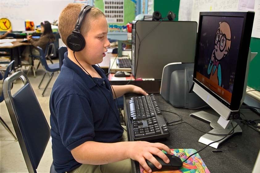 Autistic Caucasian second grade boy in school uniform wears headphones and works on computer in classroom Autistic 7 year old boy works on computer