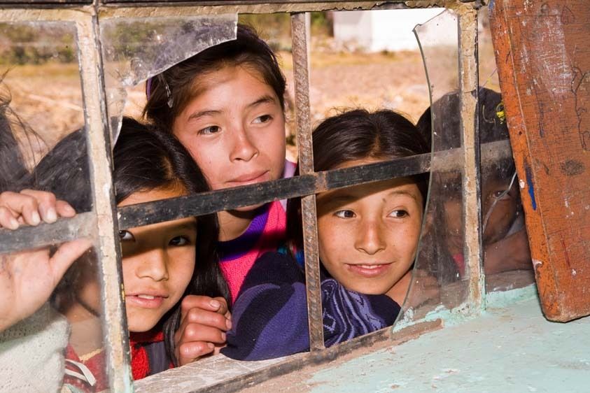 Four female students look in broken framed window of classroom in small town of Peru Peruvian school girls look in window of classroom
