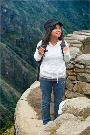 FILIPINA FEMALE-18 YEARS-WITH BACKPACK, STANDS ON ROCK WITH MACHU PICCHU IN BACKGROUND Female backpacker stands on top of Machu Picchu ruins, PERU