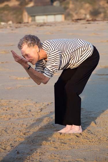 Mature woman exercises and dances on beach at sunset in Playa del Rey, Los Angeles, California Senior woman bends down to exercise at beach